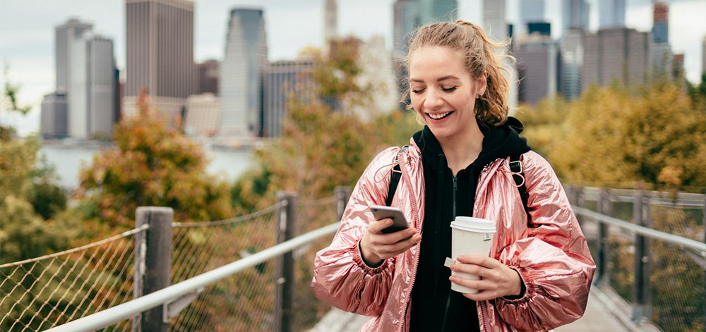A girl holding a cup of tea and looking on her phone